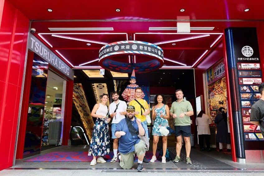 A group of people standing in front of a store with a neon sign. 4