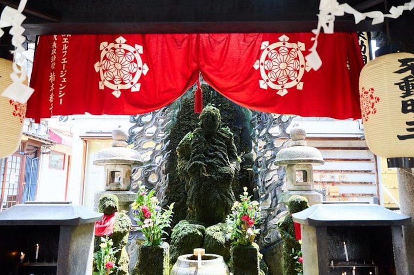 Ein Schrein mit roten Wimpeln, einer steinernen Laterne und einer Statue. 2