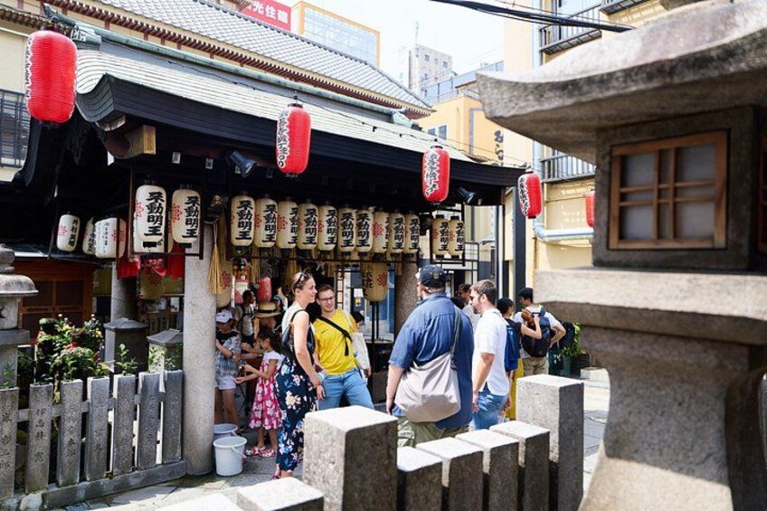 En traditionell japansk gata med stenlyktor, ett trästaket och människor som promenerar. 2