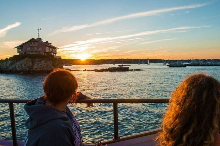 A sunset over a body of water with a house on a cliff and sailboats in the distance. 1