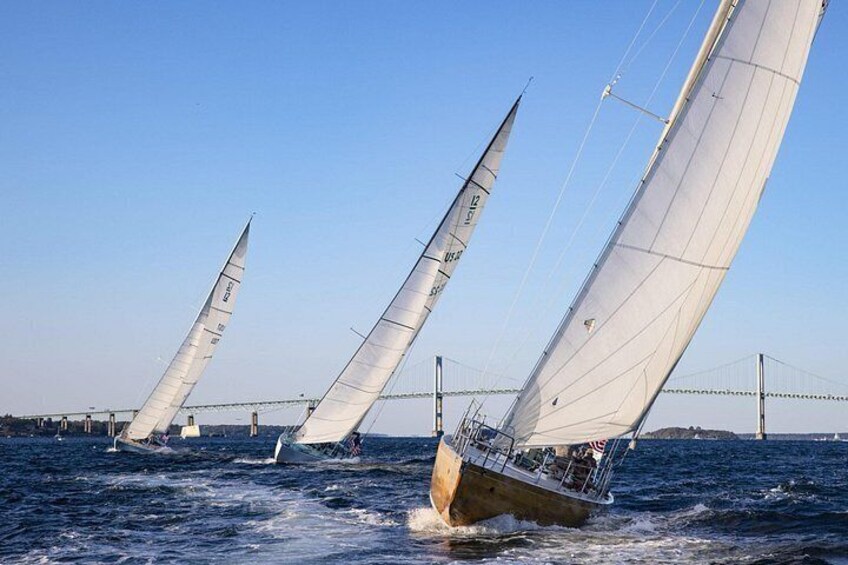 A sailboat with multiple sails on a body of water, with a bridge in the background. 4