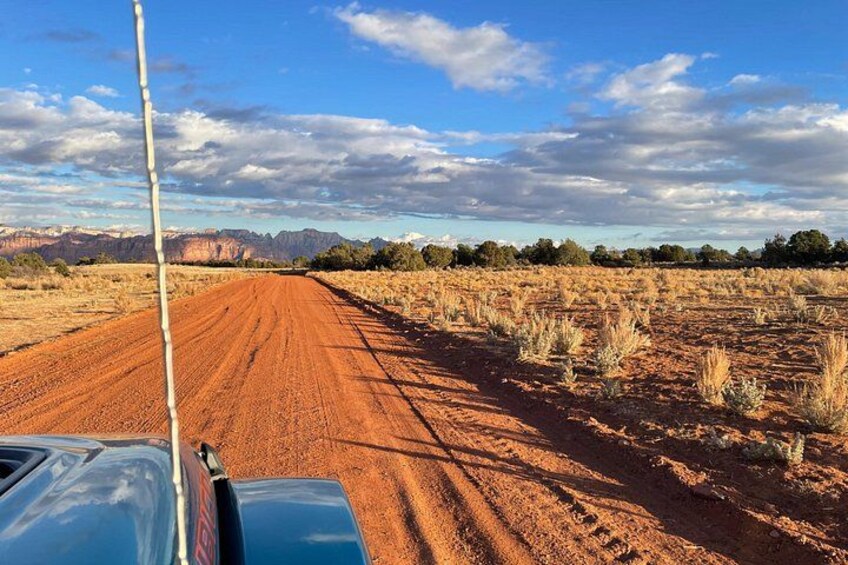 A dirt road with a blue vehicle in the foreground and a clear sky with clouds. 2