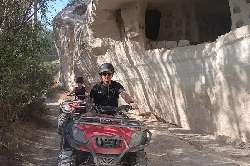Dos personas en cuatrimotos por un camino de tierra, con un risco y una estructura parecida a una cueva al fondo. 2