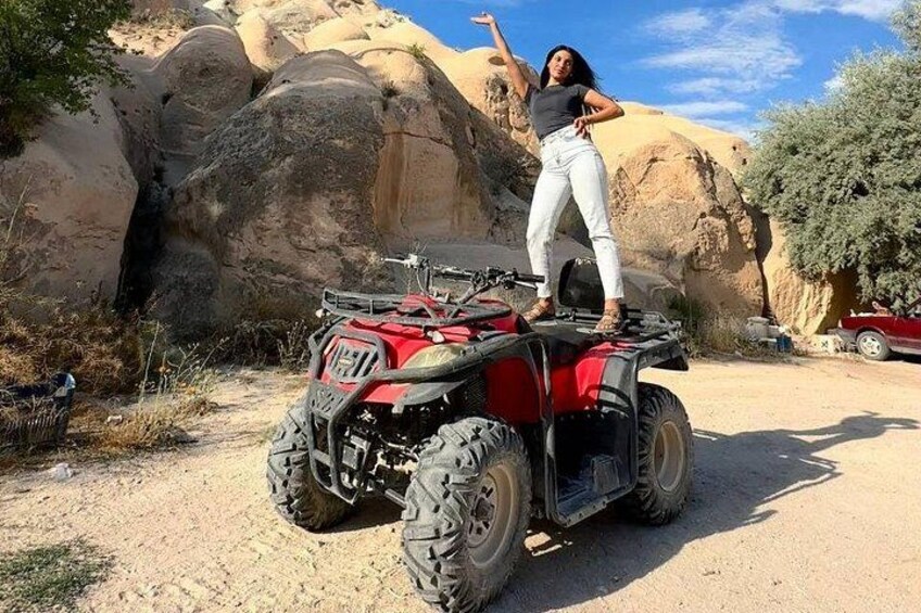 Una persona parada sobre un vehículo todo terreno rojo en un desierto con formaciones rocosas grandes al fondo. 4