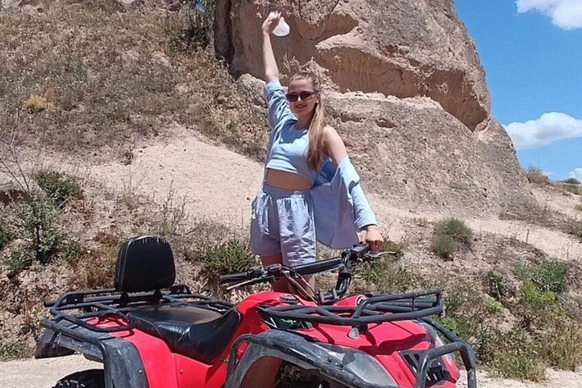 Una persona está de pie junto a un vehículo todo terreno rojo en un paisaje desértico con terreno rocoso y vegetación escasa. 5