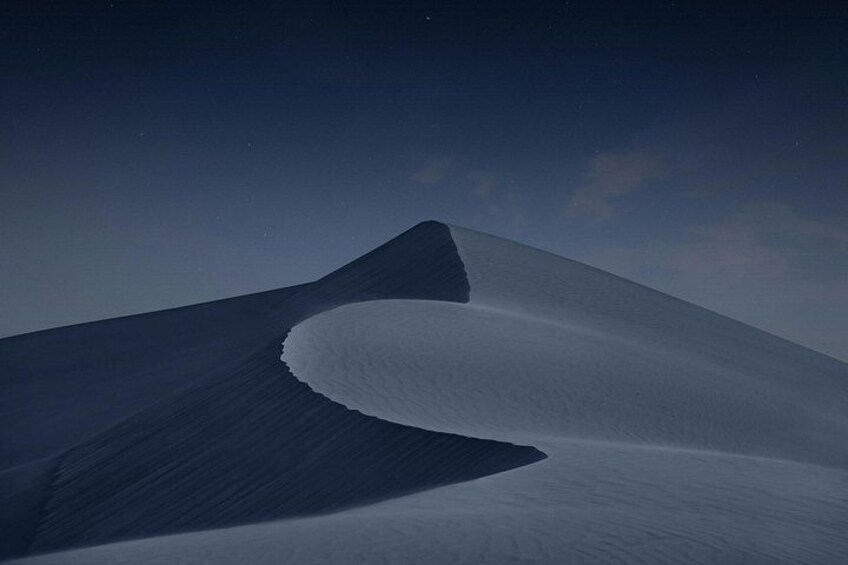 A vast desert landscape with undulating sand dunes under a starry night sky. 4