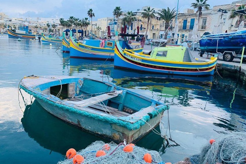 Un puerto con varias embarcaciones coloridas amarradas, redes de pesca y un cielo azul despejado. 3