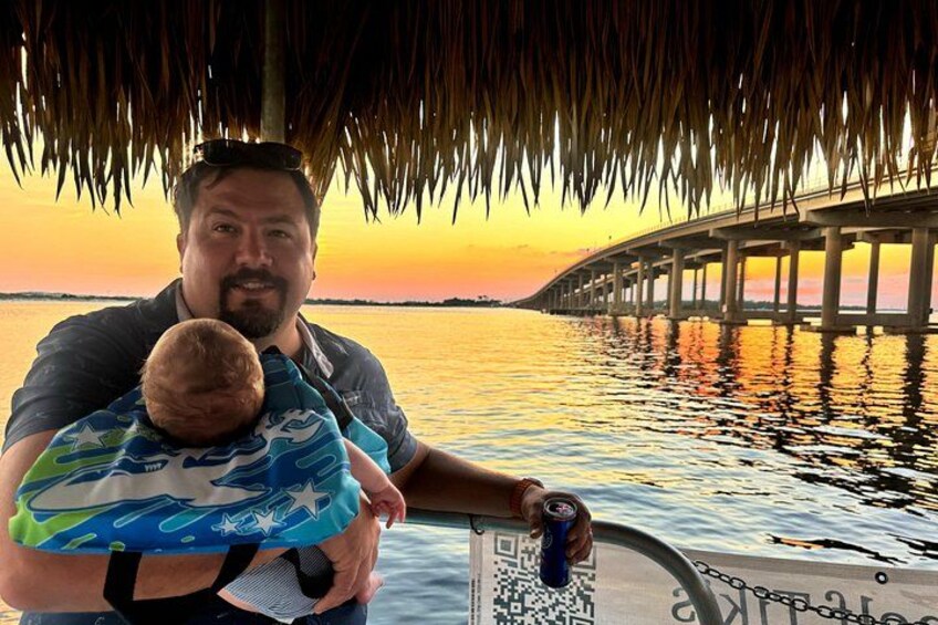 A person holding a child on a boat with a bridge in the background. 4