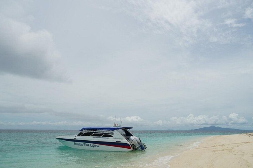 Un barco llamado 'Adaman Wave Express' en una playa con agua turquesa cristalina y una cadena montañosa distante. 3