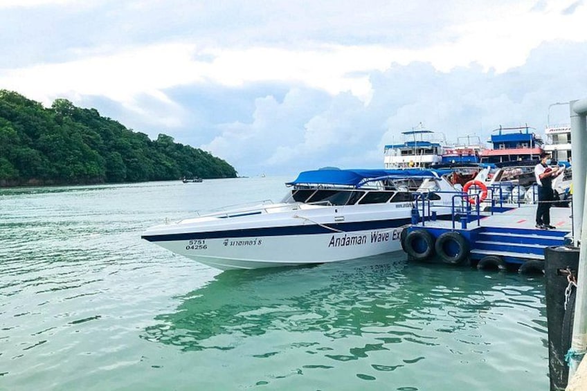 Un barco blanco llamado 'Andaman Wave Express' atracado en un muelle, con una isla cubierta de vegetación al fondo. 1