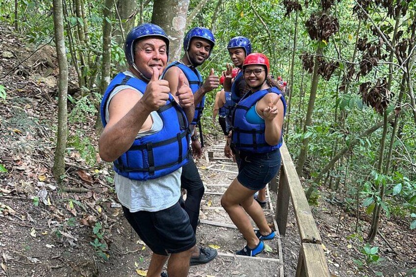 Four people wearing blue life vests and helmets on a wooden bridge in a forest. 5