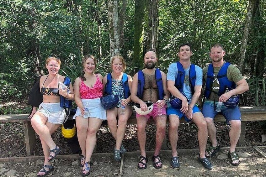A group of people sitting on a wooden bench in a forested area. 2