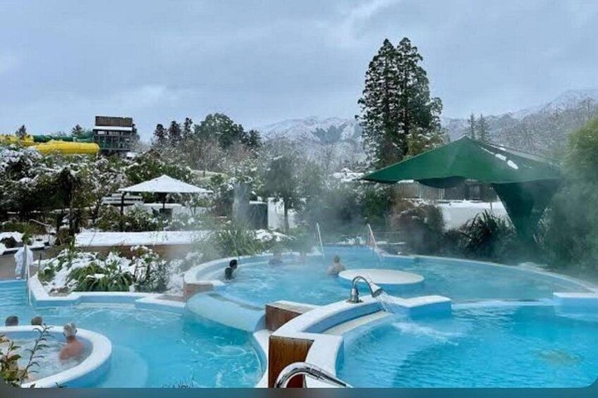 A hot spring pool with multiple smaller pools and a large central pool, surrounded by snow-covered hills and trees. 1
