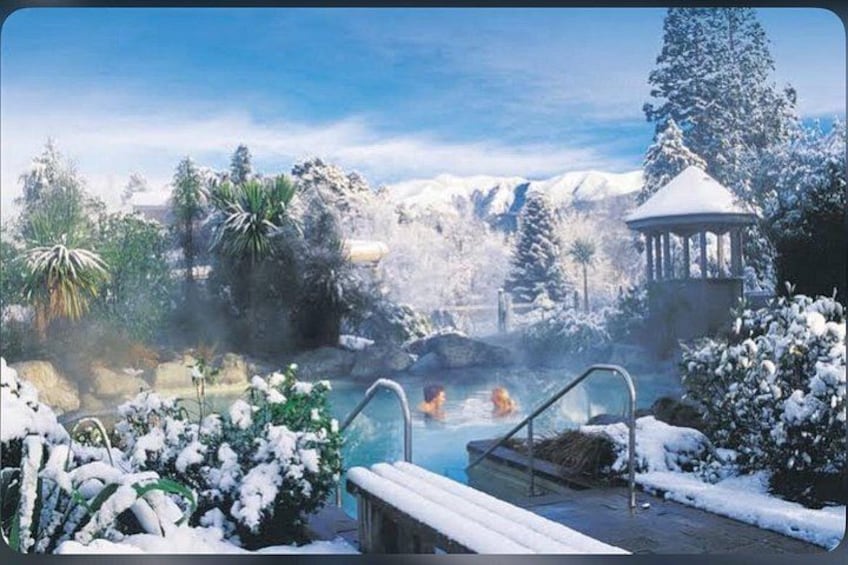 A snowy landscape with a hot spring, a gazebo, and mountains in the background. 5