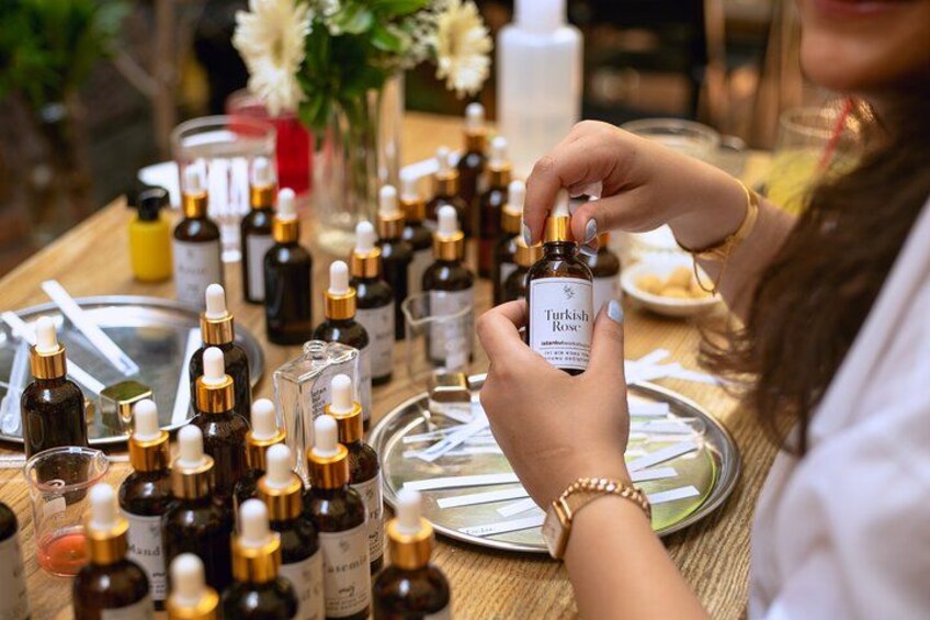 A person holding a bottle labeled "Turkish Rose" among various bottles on a table. 4