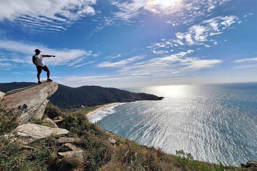 Una persona está de pie en un acantilado contemplando la costa bajo un cielo despejado. 1
