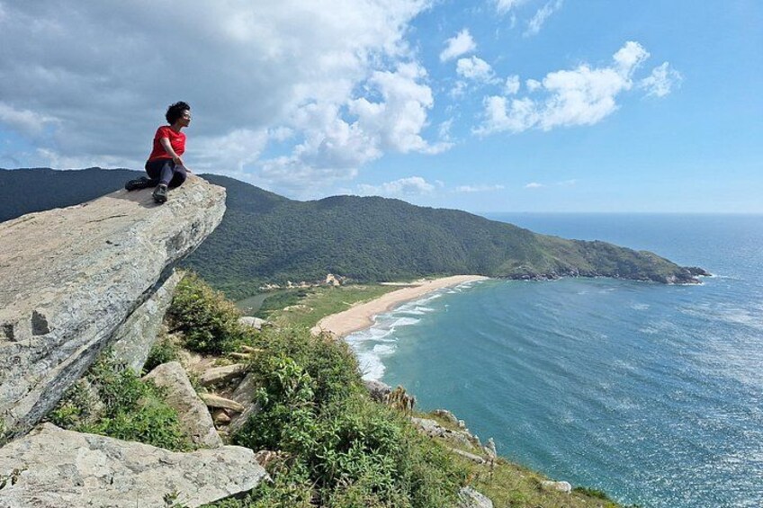 Una persona sentada en un acantilado con vistas a una playa y al océano. 2