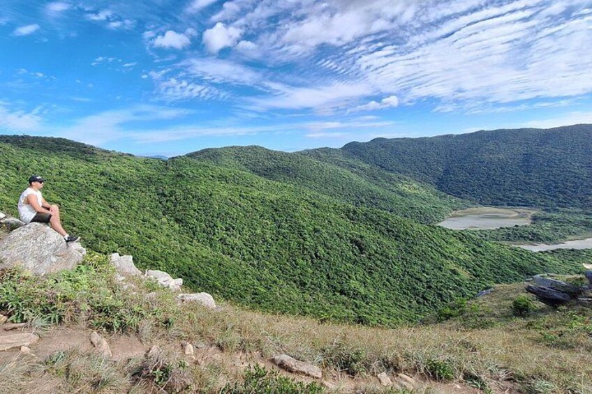 Una persona sentada sobre una roca, contemplando un valle con un bosque verde y un río. 5