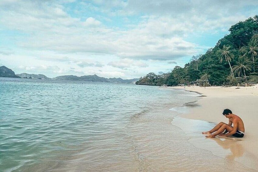 A beach with clear water, a person sitting on the sand, and palm trees in the background. 3