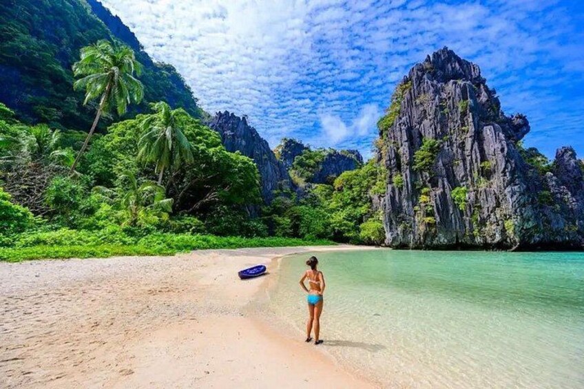 A beach with clear turquoise water, a person in a bikini, and a rocky cliff in the background. 5