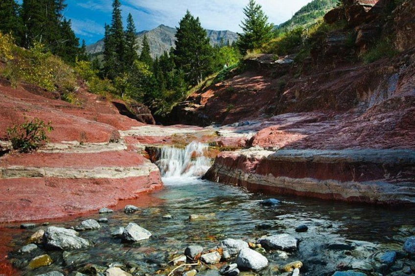 Ein roter Bach mit Wasserfall, umgeben von Bäumen und Bergen. 3