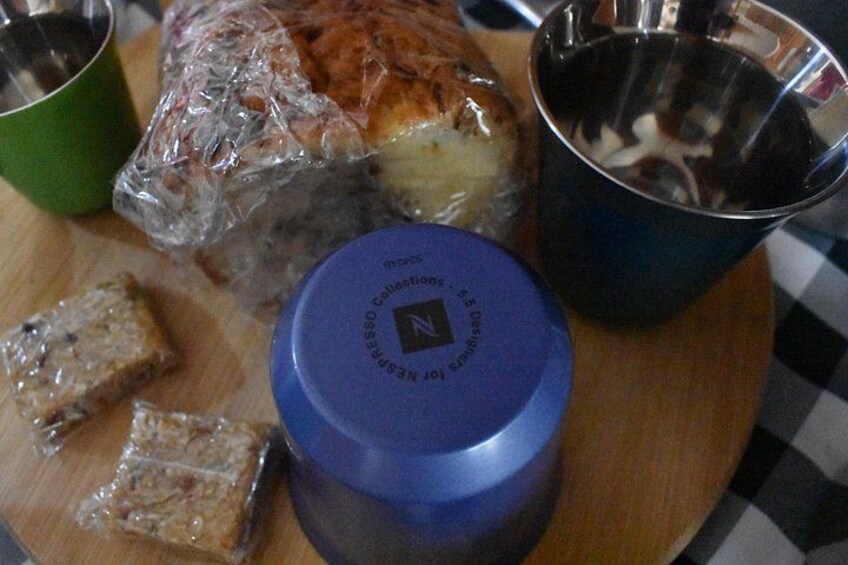 Un sándwich envuelto en plástico, un recipiente azul con un logotipo, un vaso verde y un vaso de metal sobre un mantel a cuadros. 4