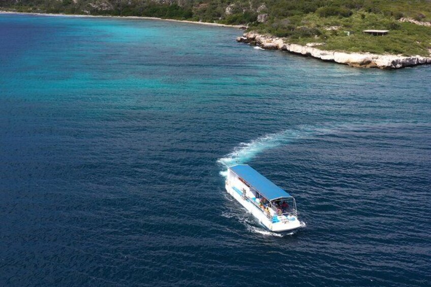 A boat traveling on a turquoise sea with a rocky coastline in the background. 2