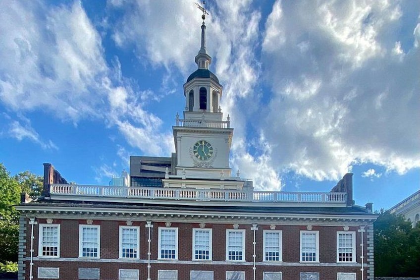 A historic building with a clock tower, a white fence, and a clear blue sky with clouds. 2