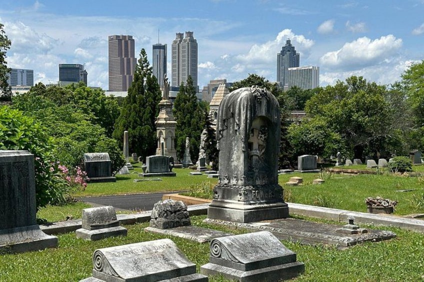 A cemetery with gravestones, a prominent statue, and a city skyline in the background. 4