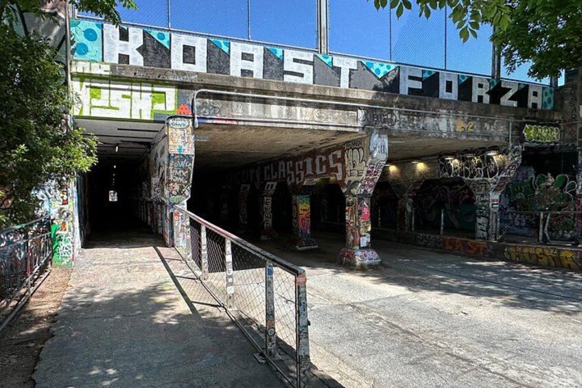An underground passageway under a bridge with graffiti and a metal fence. 3