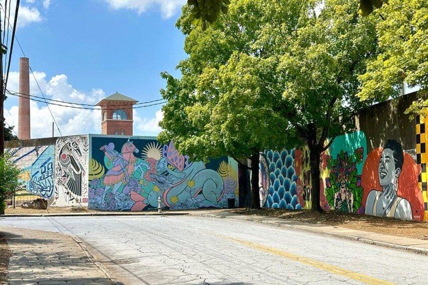 A street with colorful murals on the walls, a clock tower, and trees. 2