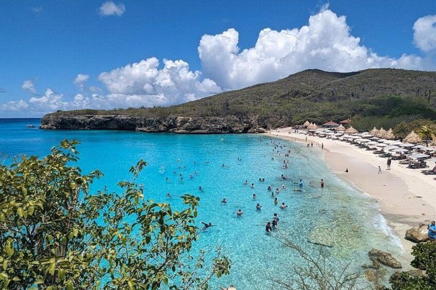 A beach with clear turquoise water, people swimming, and a rocky coastline. 2