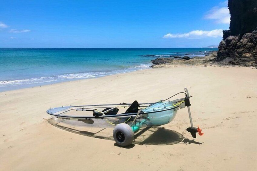 A glass-bottomed boat on a sandy beach with clear blue water and a rocky cliff in the background. 1