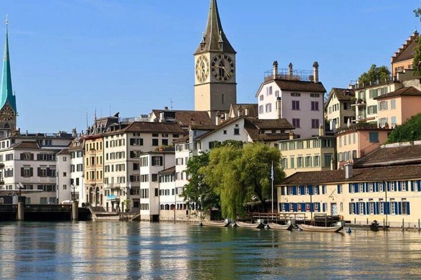 A riverside town with historic buildings, a clock tower, and a church spire. 2