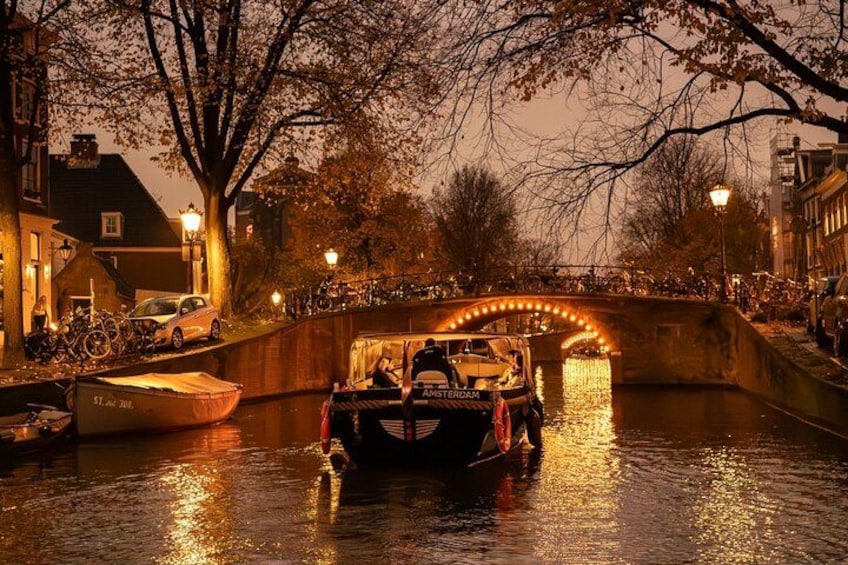 A canal with a boat passing under a bridge, surrounded by buildings and trees. 5