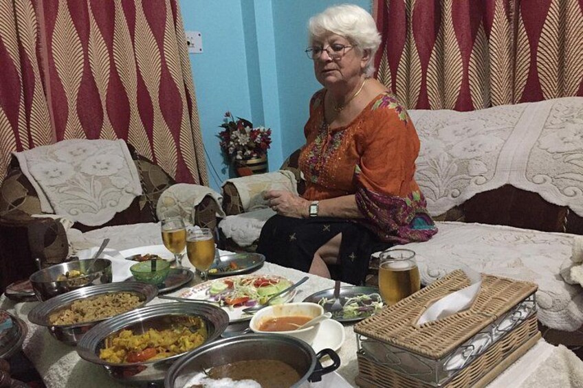 An elderly woman sitting on a couch with a table full of food and drinks in front of her. 2