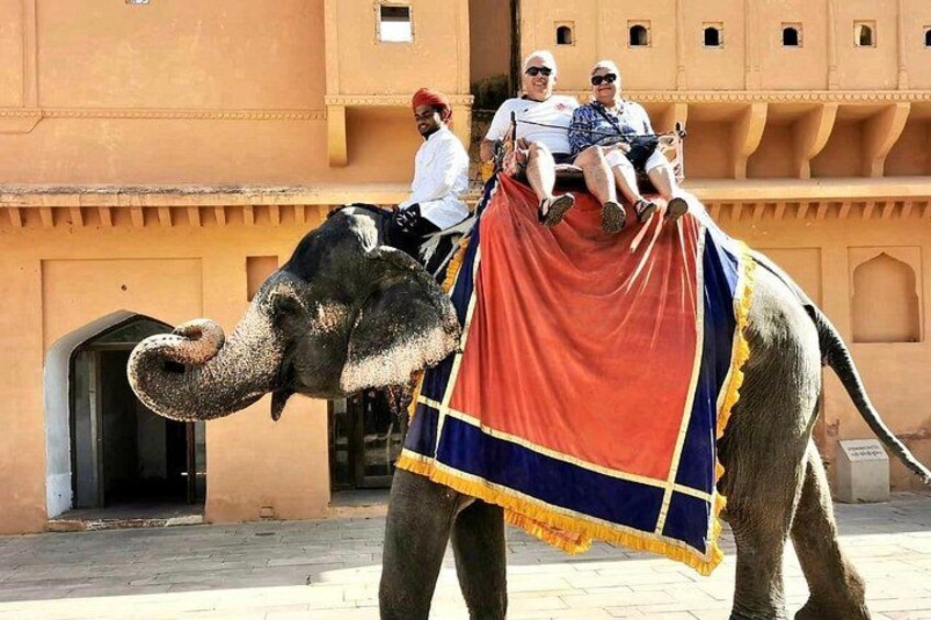 An elephant with a rider and two passengers, a building with traditional architecture in the background. 4