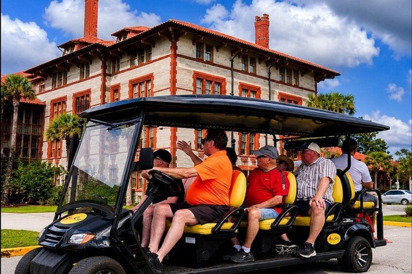 A golf cart with passengers, a building with red and white trim, and a clear blue sky. 1