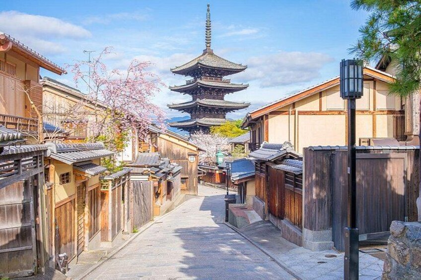 A traditional Japanese street with wooden houses, cherry blossoms, and a pagoda in the distance. 2