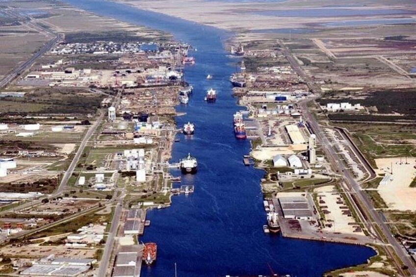 An industrial port with multiple ships docked along a narrow waterway, surrounded by industrial buildings and infrastructure. 2