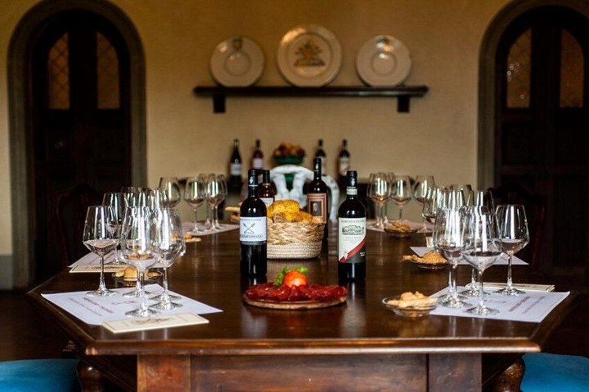 Une table à manger dressée pour une dégustation de vins, avec des verres à vin, des bouteilles et un panier de fruits. 1