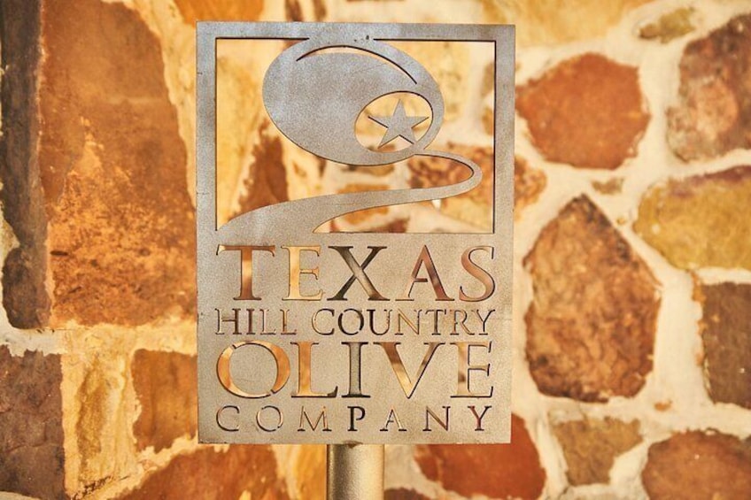 Un letrero con el texto 'TEXAS HILL COUNTRY OLIVE COMPANY' sobre un fondo de pared de piedra. 5