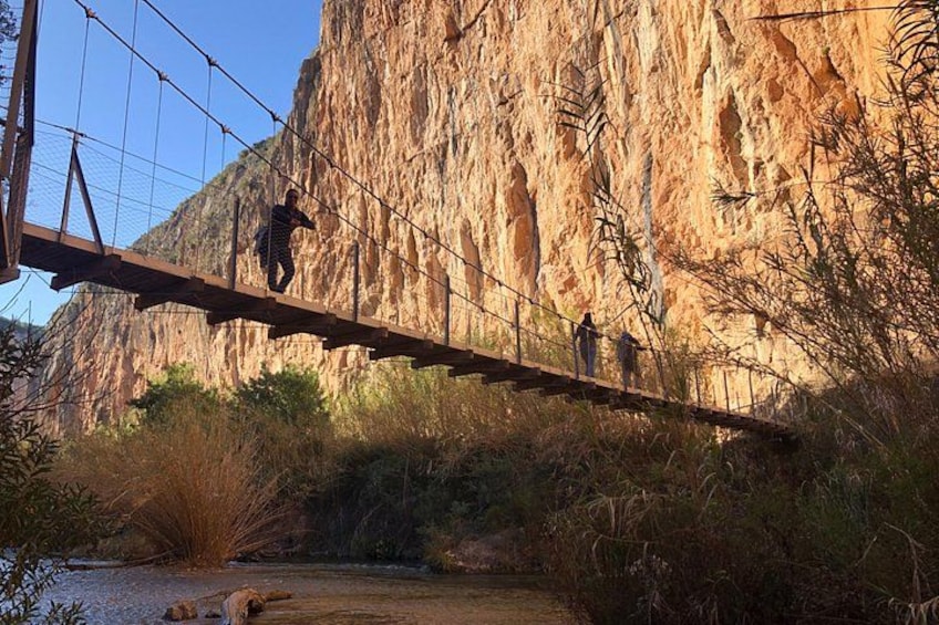 A suspension bridge over a river with a rocky cliff in the background. 2