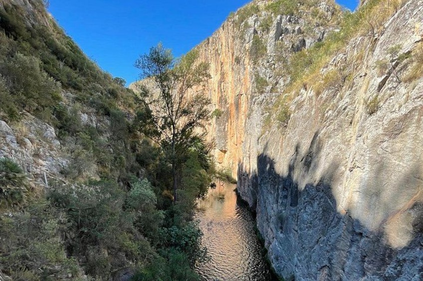 A canyon with a narrow water channel, rocky cliffs, and sparse vegetation. 3