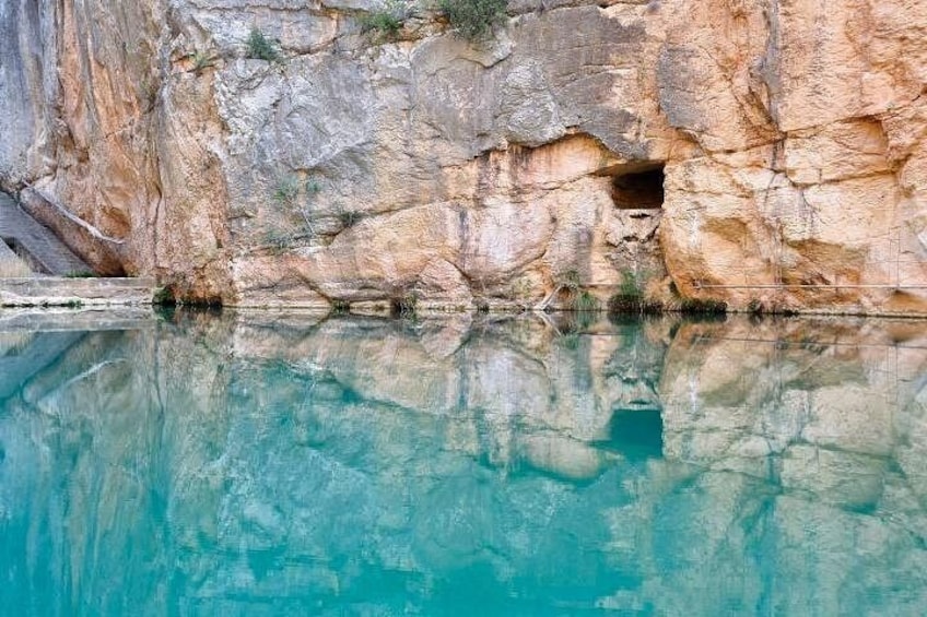 A clear turquoise pool reflecting a rocky cliff. 1
