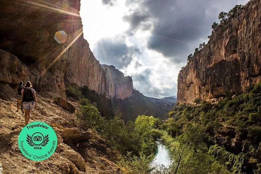 A canyon with a river, rocky cliffs, and hikers. 1