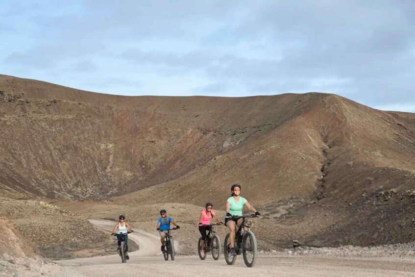 Four cyclists on a dirt road in a hilly, arid landscape. 3