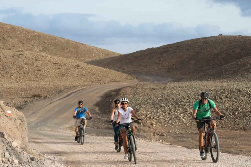 A group of cyclists on a dirt road in a hilly, arid landscape. 2