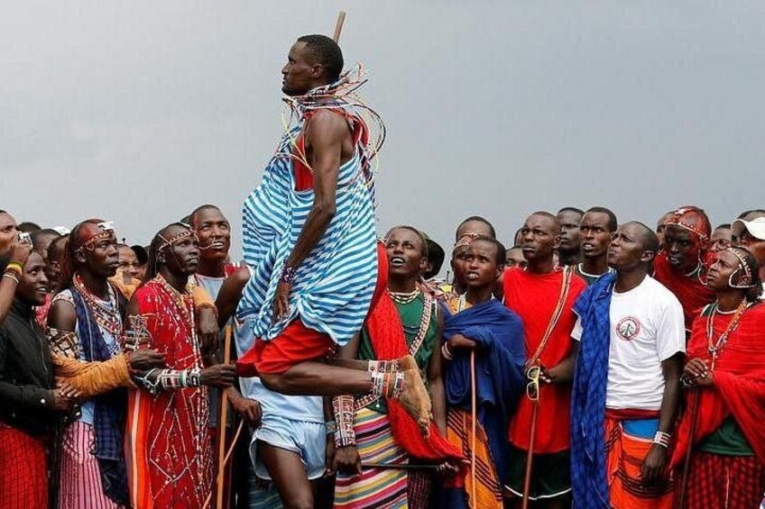 A group of people in traditional attire, some holding objects, gathered in a semi-circle. 2