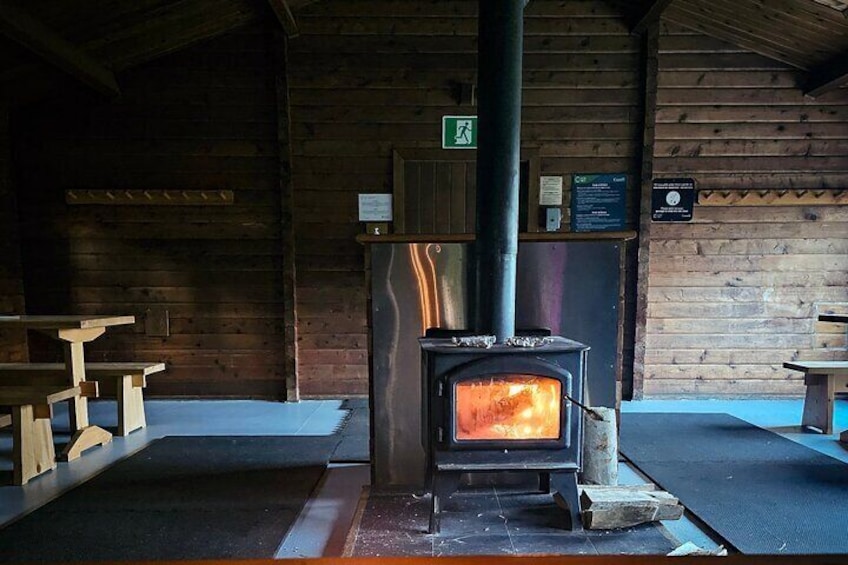 A wood-burning stove in a rustic cabin with wooden benches and a sign on the wall. 4